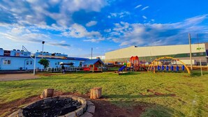 A playground with slides and swings, a small red house, and a large building labeled "ALP 1" in the background.