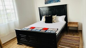 Een slaapkamer met een zwart bed, witte beddengoed, een kleurrijk vloerkleed, een houten nachtkastje en een schilderij aan de muur.