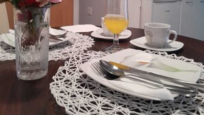 Una mesa de comedor dispuesta con un florero, un vaso de jugo de naranja y una taza blanca.