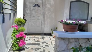 Un estrecho acceso adoquinado con una puerta blanca, plantas en macetas y una pared de piedra.