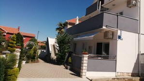 Un edificio moderno de dos pisos con balcón, antena parabólica y entrada pavimentada.