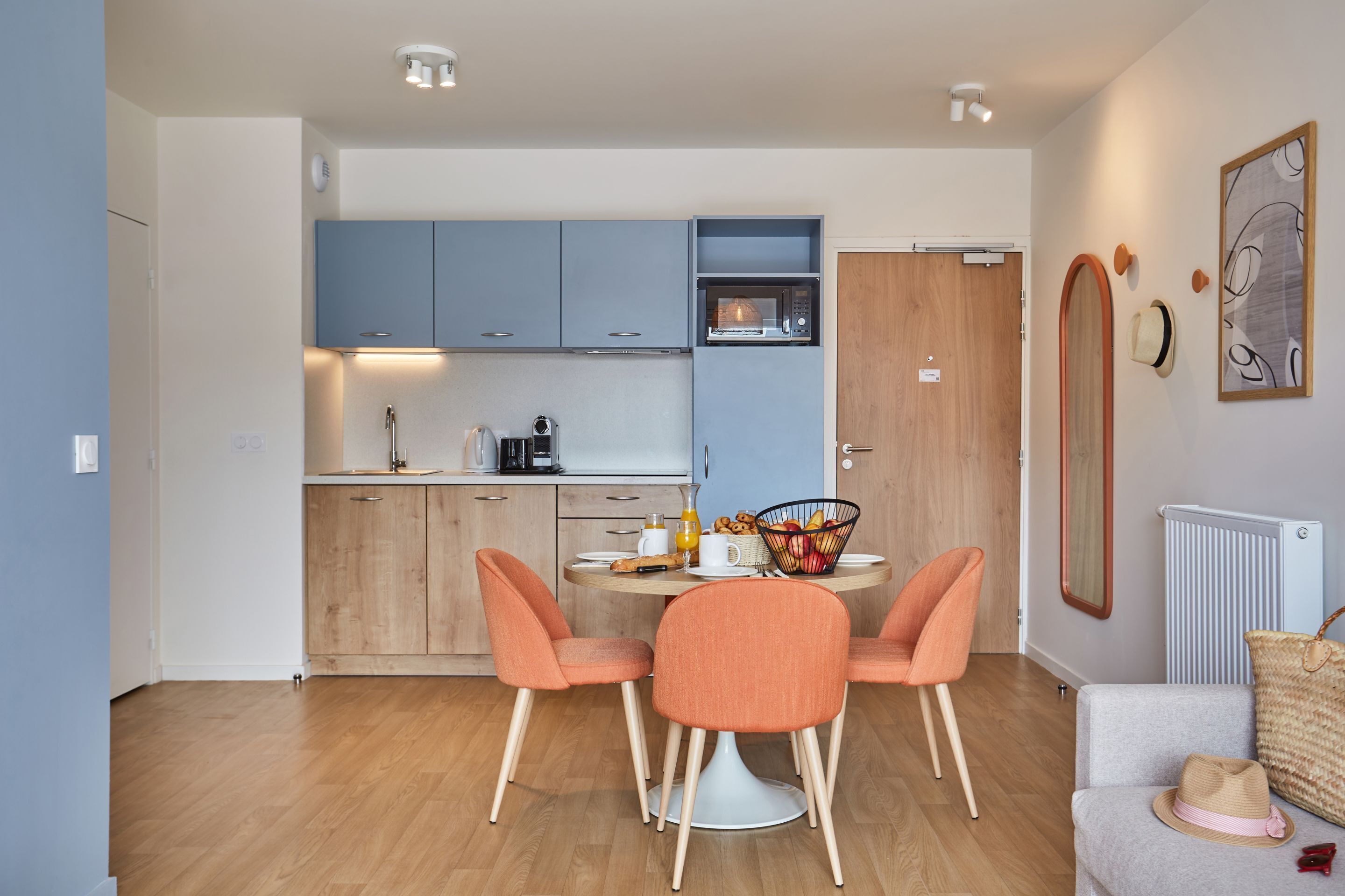 A modern kitchen with blue cabinets, a microwave, and a dining area with orange chairs and a white table.