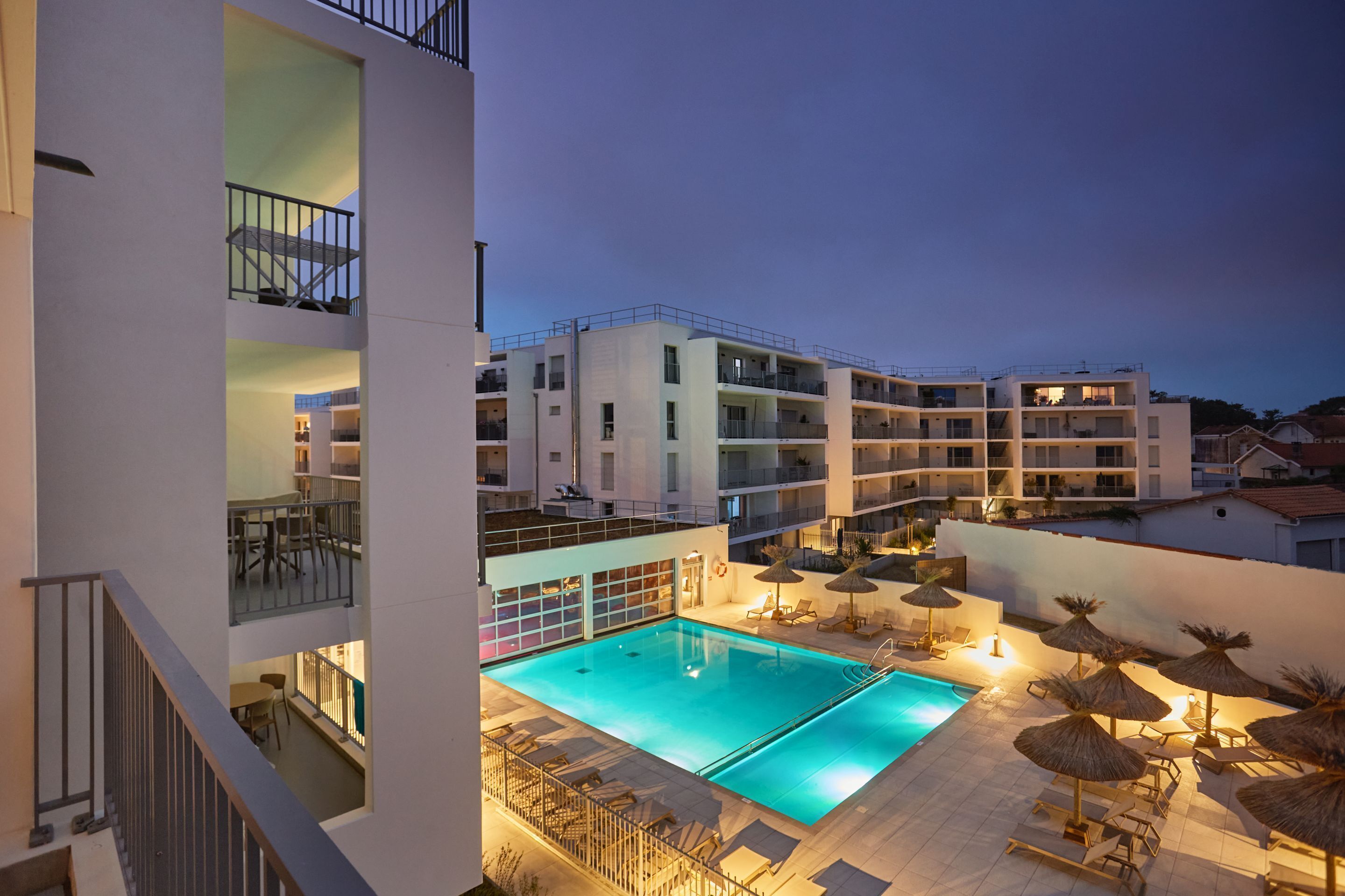 A modern hotel with a rooftop pool, outdoor seating, and a view of the surrounding buildings.