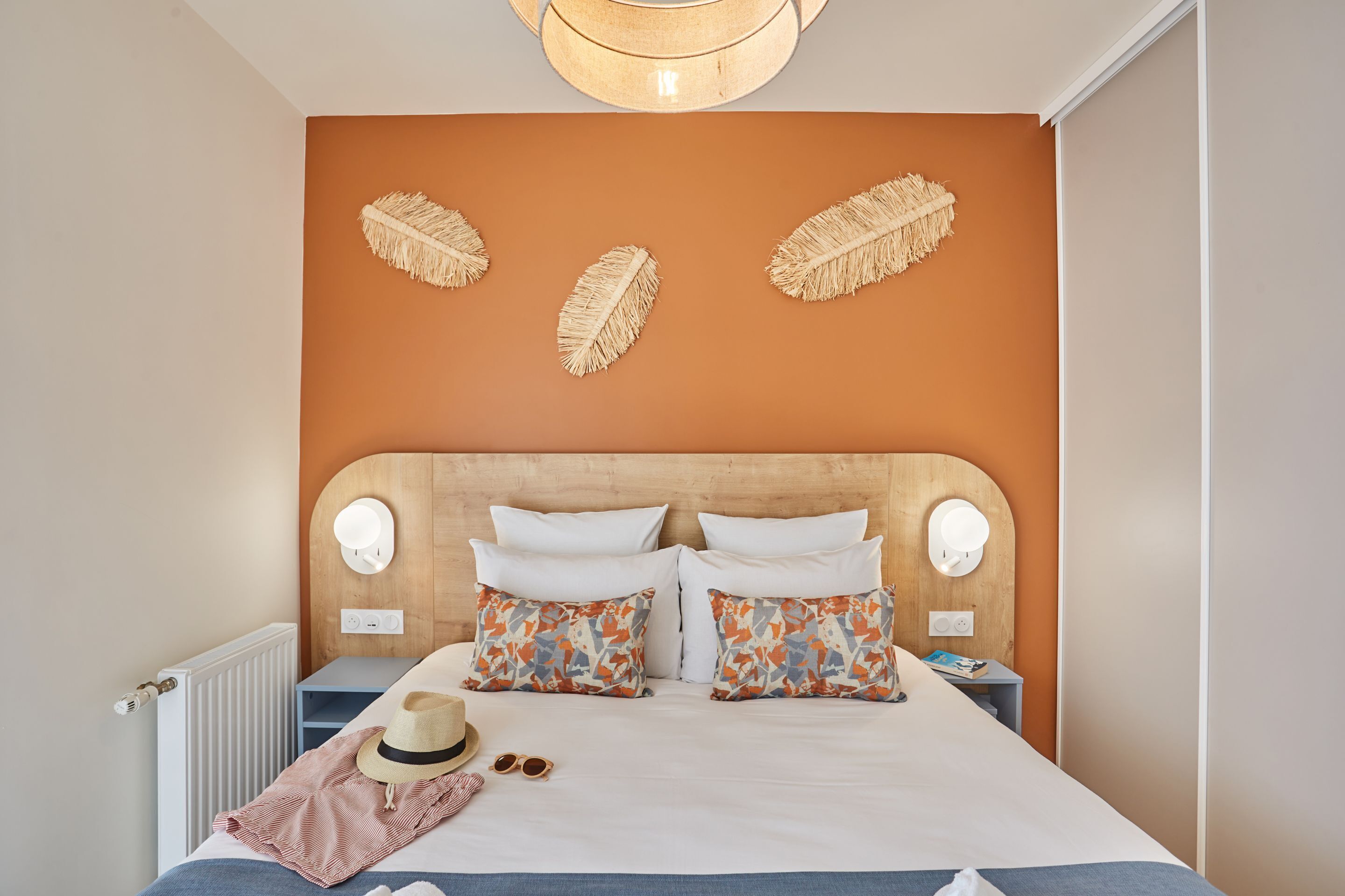 A neatly made bed with patterned pillows, a wooden headboard, and a wall-mounted light fixture.