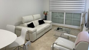 A modern living room with a white leather sofa, a glass coffee table, and a round dining table with chairs.