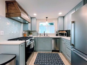 A modern kitchen with grey cabinets, a stainless steel refrigerator, a microwave, and a stove.