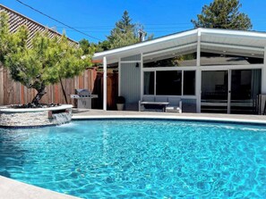 A swimming pool with a covered patio area, a wooden fence, and a tree.