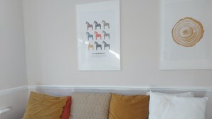 A room with a light-colored sofa against a wall, adorned with a framed picture of horses and a circular design. - Spacious 3-bed House in Brighton With Parking (Brighton)