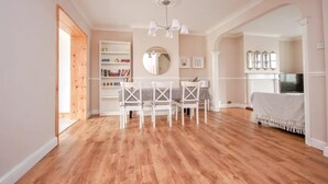 A spacious room with a wooden floor, a dining area with white chairs, a bookshelf, and a fireplace. - Spacious 3-bed House in Brighton With Parking (Brighton)