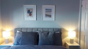 A bedroom with a grey upholstered headboard, two framed pictures on the wall, and bedside lamps on either side of the bed. - Spacious 3-bed House in Brighton With Parking (Brighton)