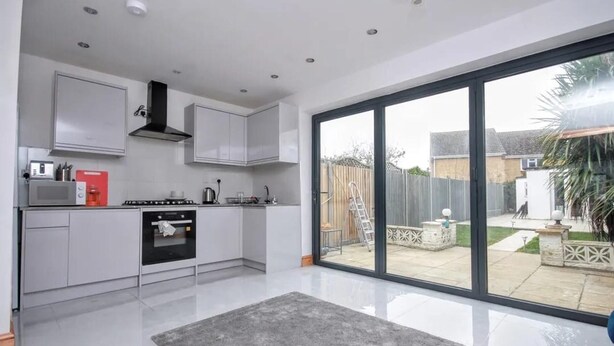 A modern kitchen with white cabinets, a stove, and a large sliding glass door leading to a backyard. - Spacious 3-bed House in Brighton With Parking (Brighton)