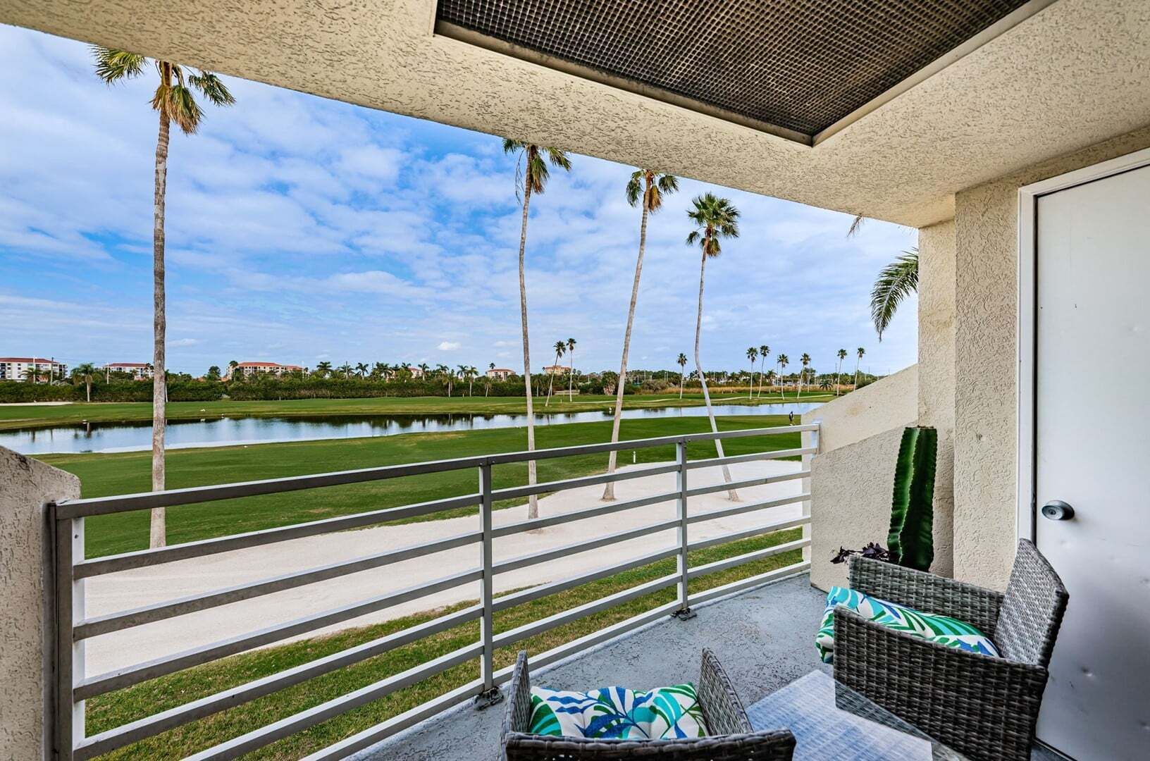 A balcony with a view of a golf course, palm trees, and a body of water.