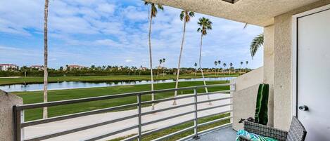 A balcony with a view of a golf course, palm trees, and a body of water.