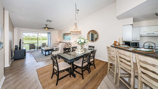 A spacious living area with a dining table, chairs, and a chandelier. There is a kitchen area with a microwave and cabinets. - VVN 5-229 - Vista Verde North - Premium (St. Petersburg)