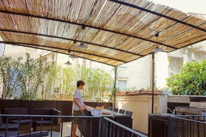 Een terras buiten met een bamboe overkapping, zitplaatsen en iemand die een dienblad draagt.