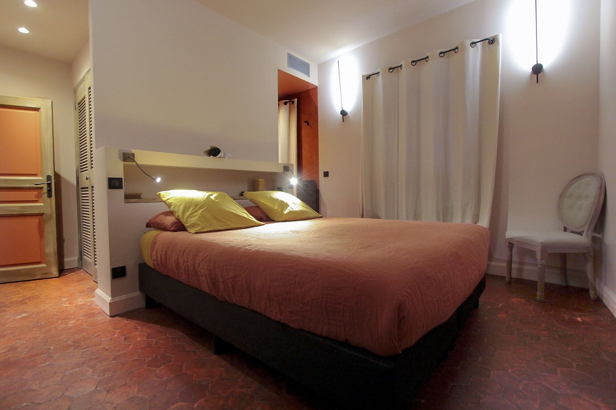 Une chambre à coucher avec un lit, une chaise, un miroir et une fenêtre avec des rideaux.