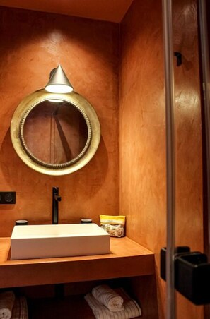 Een badkamer met een houten wastafelmeubel, een ronde spiegel en een handdoekrek.
