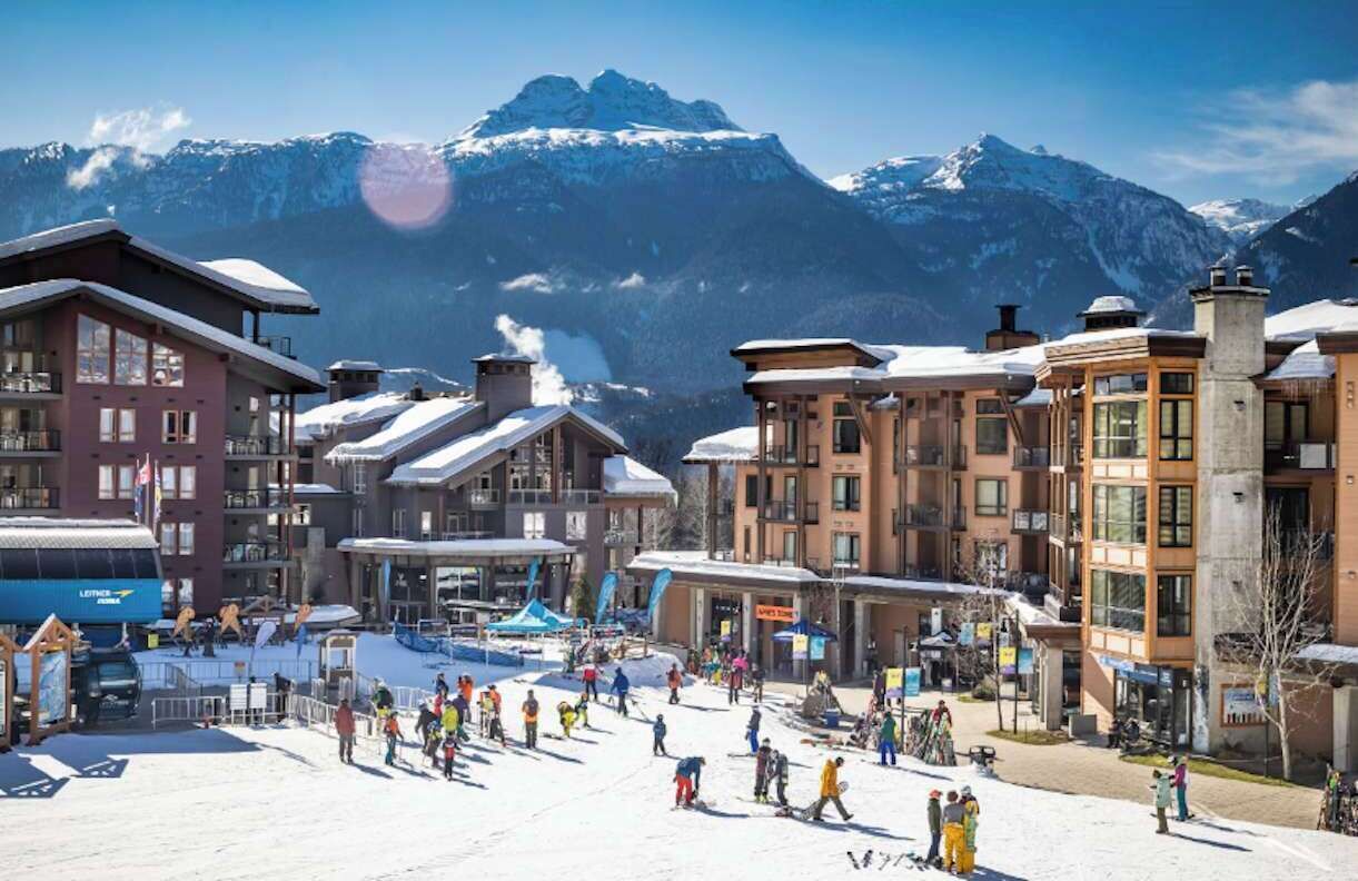 Een skigebied met gebouwen, een kabelbaan en een besneeuwde berg op de achtergrond.