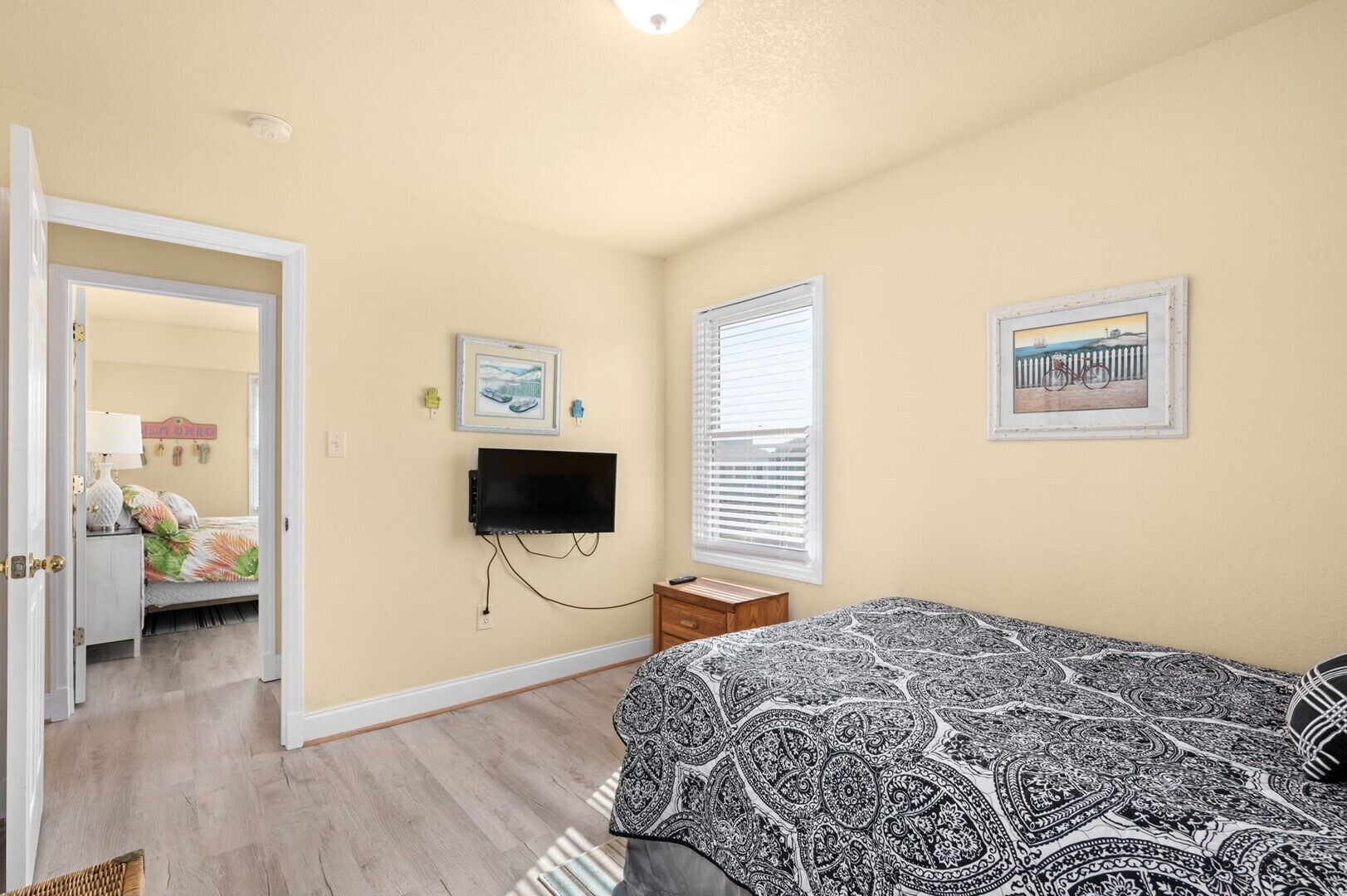 A bedroom with a bed, a TV, a window, and a door leading to another room.