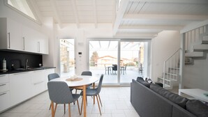 Une cuisine moderne avec des meubles blancs, une table à manger avec des chaises et un canapé gris.