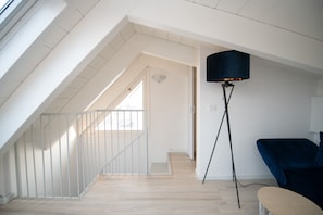 A spacious room with a sloped ceiling, a wooden floor, a black floor lamp, and a blue chair.