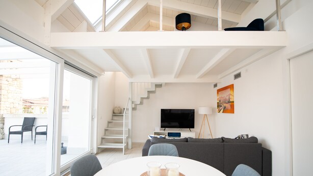 Un salon moderne avec un plafond blanc, un canapé gris, un téléviseur et une table à manger avec deux verres.