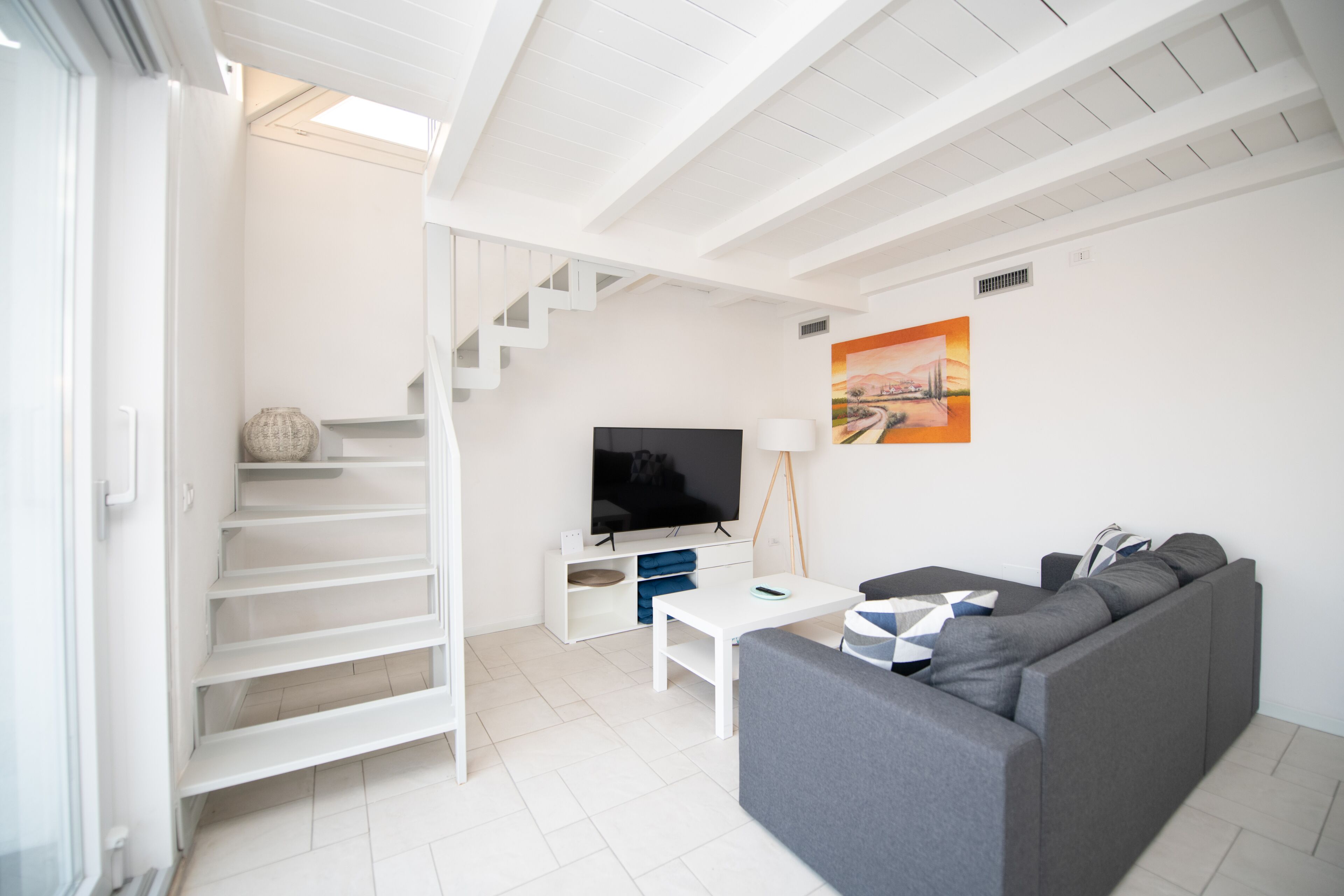 Una sala de estar moderna con una escalera, un televisor de pantalla plana, un sofá y un cuadro en la pared.