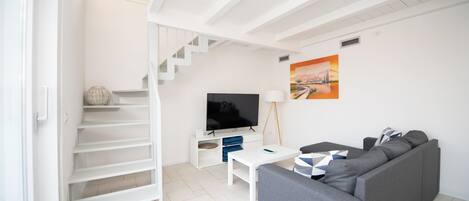 Una sala de estar moderna con una escalera, un televisor de pantalla plana, un sofá y un cuadro en la pared.