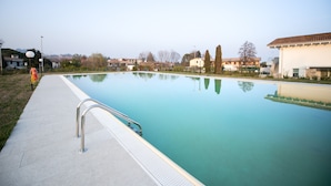 Une piscine dotée d’une rambarde métallique, entourée d’une terrasse en béton et surplombée par un ciel dégagé.