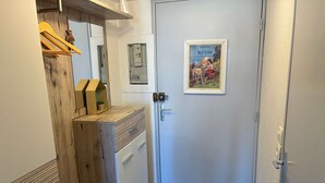 Een hal met een houten bankje, een deur met een poster en een lichtschakelaar aan de muur.