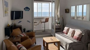 Un salon avec un canapé, des fauteuils, un téléviseur et une vue sur la mer.