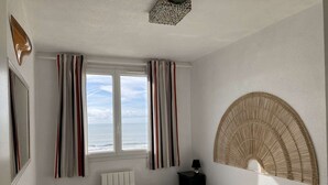 Une chambre à coucher comprenant un lit, un radiateur, une table de chevet, une lampe, une fenêtre avec des rideaux et un objet décoratif fixé au mur.