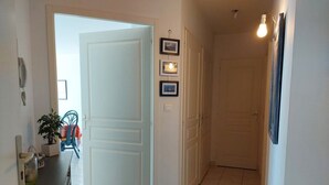 Un pasillo con una puerta cerrada, una mesita con una planta y un aplique de pared.