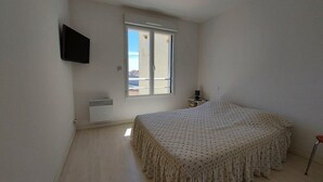 Un dormitorio con cama, televisión montada en la pared, ventana y una mesita de noche.