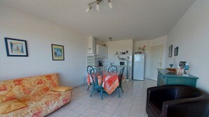 Una sala de estar con un sofá, una mesa de centro y un comedor con sillas y una mesa. Hay una zona de cocina con un refrigerador y un microondas.
