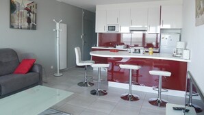 Een knus woongedeelte met een kitchenette, een bank, een bijzettafeltje en een bar met krukjes.