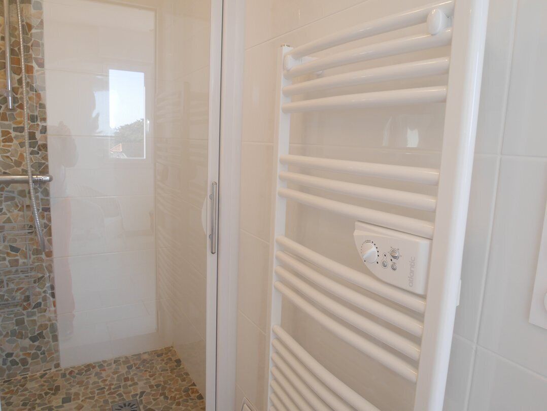 A bathroom with a glass shower enclosure, a white tiled shower area, and a white towel rack with a control panel.