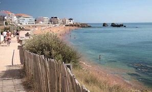 A coastal beach with a wooden walkway, beachgoers, and buildings in the background.