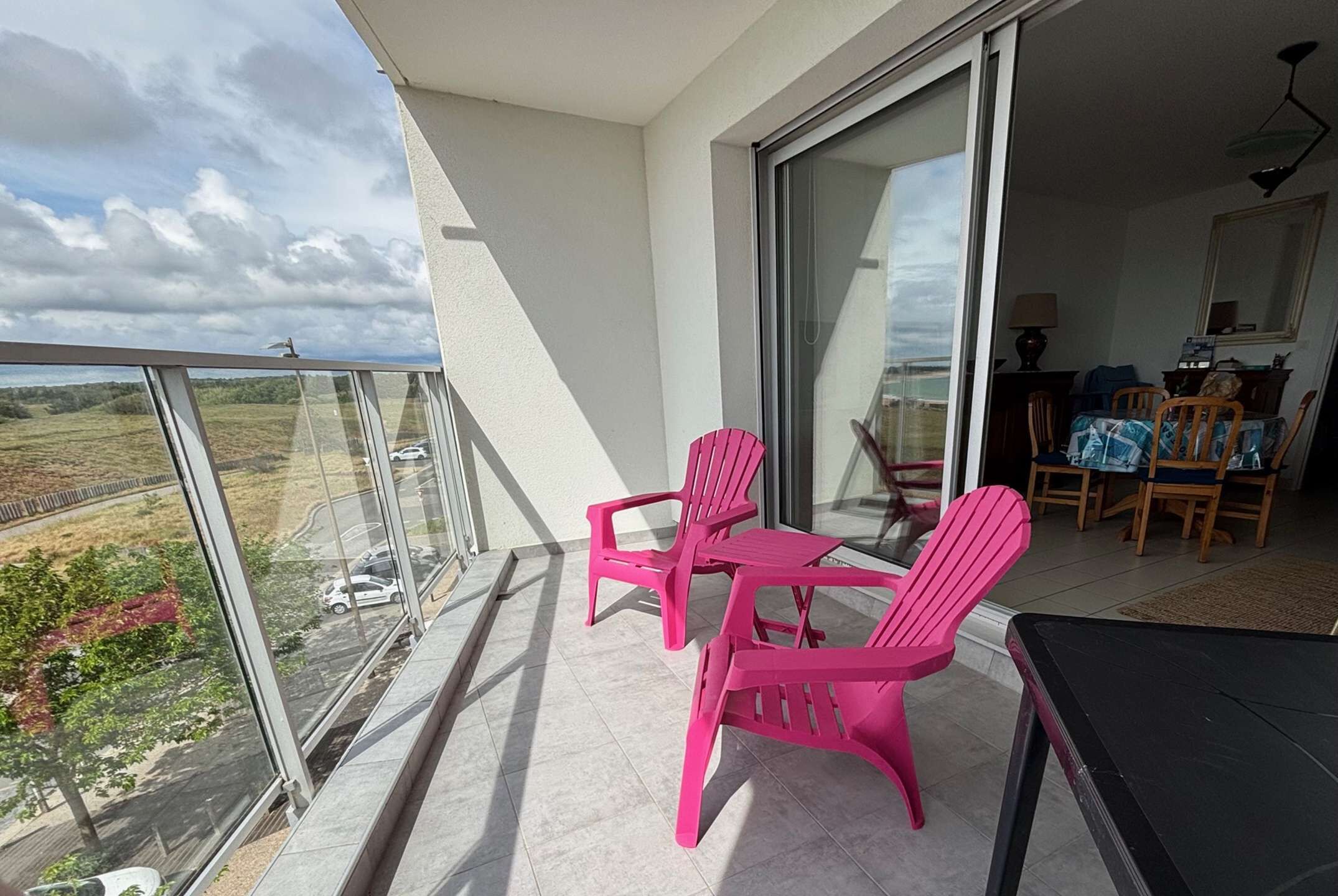 Un balcon avec une table et des chaises, une vue sur la campagne et un coin repas à l’intérieur.