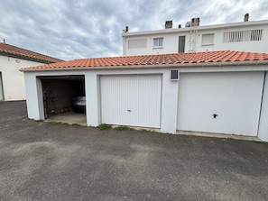 Um edifício térreo com garagem, um carro estacionado no interior e telhado com telhas vermelhas.
