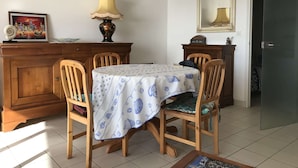 Un coin repas avec une table recouverte d’une nappe, des chaises en bois, une lampe, un tableau et un miroir au mur.