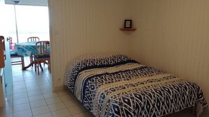 Une chambre avec un lit, une petite étagère et un coin repas comprenant des chaises et une table.
