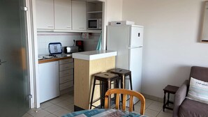 Une cuisine compacte avec des meubles blancs, un four à micro-ondes, un réfrigérateur et un petit coin repas équipé de tabourets.