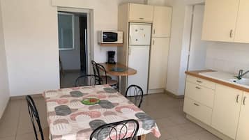 Une cuisine compacte comprenant une table à manger, des chaises, un four à micro-ondes, un réfrigérateur et un évier.