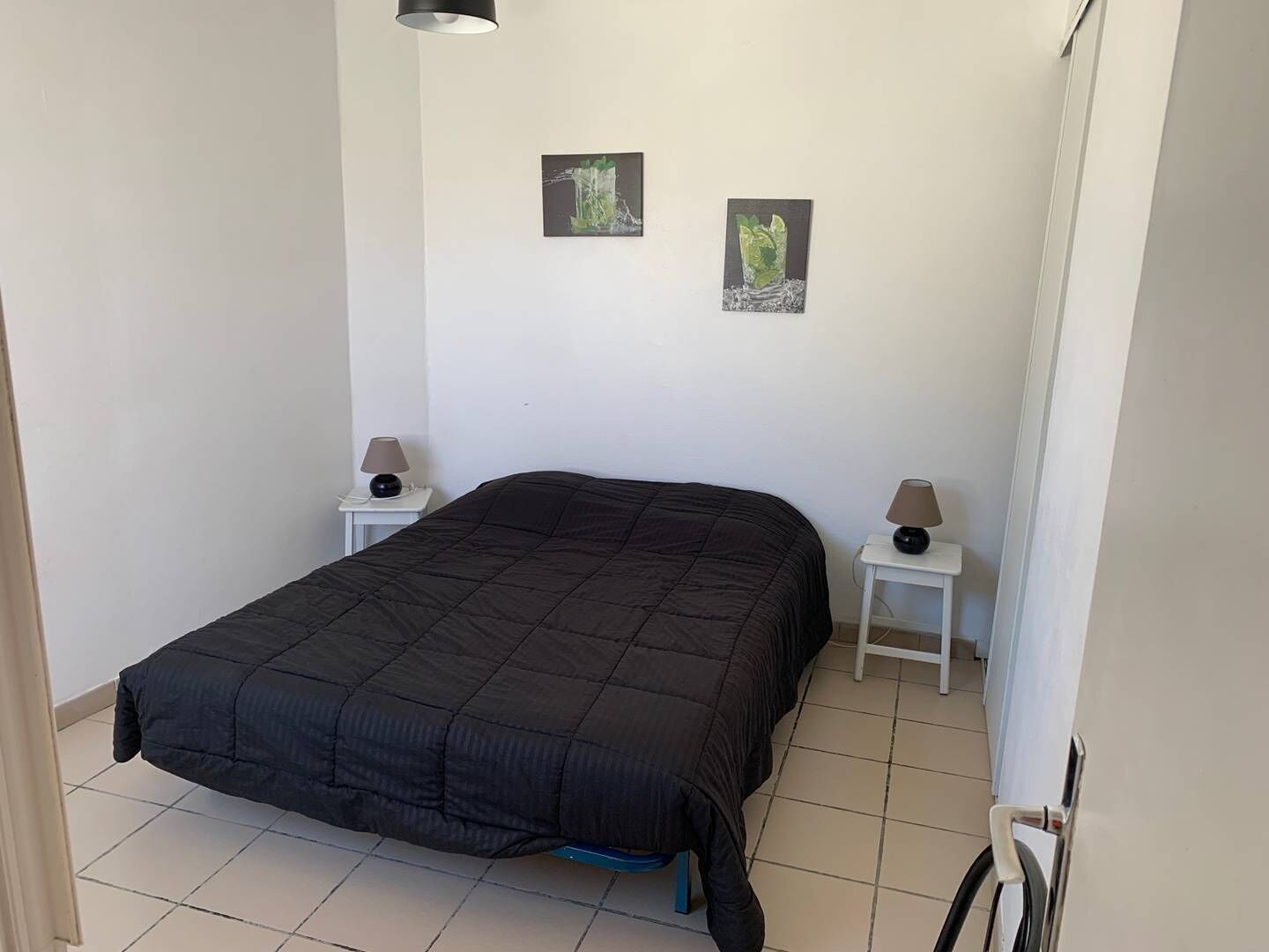 Une chambre avec un grand lit, deux tables de chevet avec des lampes et deux tableaux encadrés accrochés au mur.