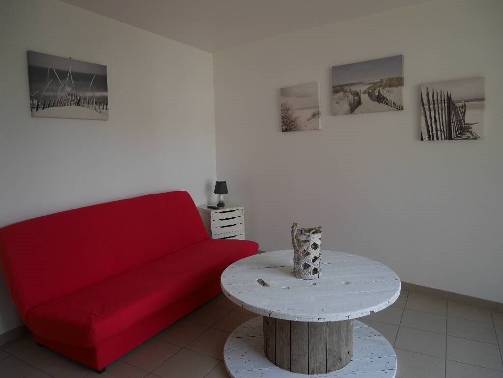 Een kamer met een rode bank, een ronde witte tafel met een decoratieve vaas, en drie ingelijste foto's aan de muur.
