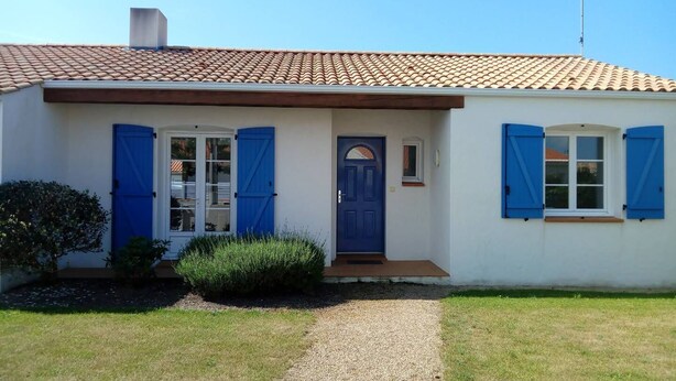 A single-story house with a tiled roof, a front door, and two windows with blue shutters.