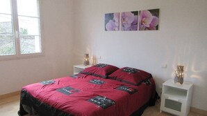 A bedroom with a large bed, two bedside tables, a window, and three wall-mounted flower paintings.
