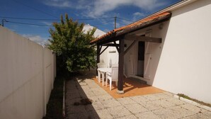 A small patio area with a white table and chairs, a tiled floor, and a white wall. - La tranquille - St Hilaire de Riez (SAINT HILAIRE DE RIEZ)