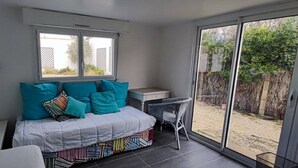 A bedroom with a bed, a desk, and a view of the backyard through a sliding glass door. - La Nantaise de la mer Saint Hilaire de Riez (SAINT HILAIRE DE RIEZ)
